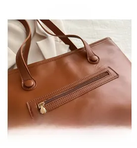 Detailed close-up of brown tote bag showing litchi grain texture and metal zipper pocket