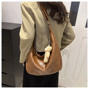 Brown leather hobo bag with wide strap and cute plush bear charm on a female model
