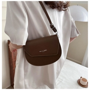 Close-up of brown saddle bag with FASHION TREND text worn by model on white top