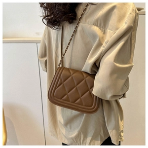 Detailed view of a brown quilted PU leather shoulder bag with gold chain strap on model