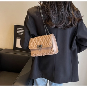 Detail of apricot quilted crossbody bag featuring V-shaped metal lock and chain strap