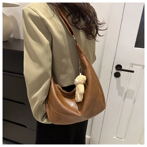 Detail of brown leather crescent bag with shoulder strap and plush bear charm