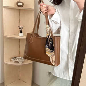 Detail of a brown leather tote bag with vintage printed silk scarf on light background