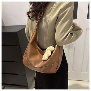 Detail of a brown vintage half-moon shoulder bag with a cute plush bear charm decoration