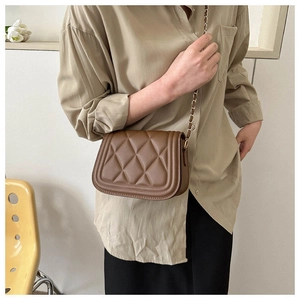 Detail of brown quilted crossbody bag with golden leather-woven chain strap worn on shoulder