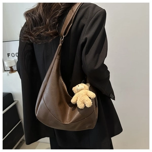 Hobo bag in dark brown leather with cute teddy bear plush pendant on a black blazer