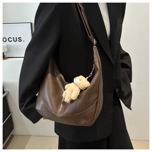 Detail of dark brown croissant bag with a cute beige plush bear pendant on shoulder strap