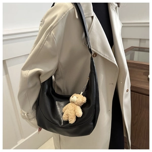 Detail of black leather dumpling bag with cute plush bear pendant on beige trench coat