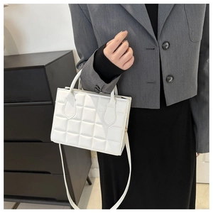 Close-up of white quilted leather handbag featuring detailed square stitching and handles