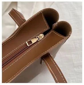 Detail of a brown leather tote bag showing smooth golden zipper and white contrast stitching