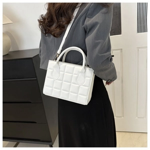 Rear view of model wearing white quilted handbag with cross-body strap on grey blazer
