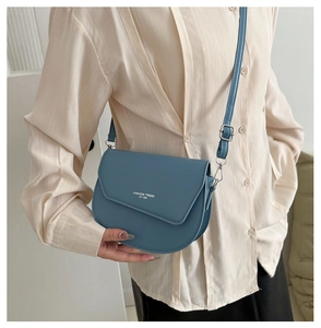 Detail view of a blue matte leather saddle bag featuring white fashion trend typography