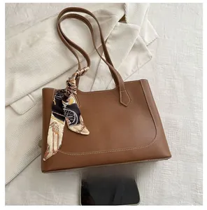 Brown leather tote bag detail with decorative floral scarf and smartphone for size reference