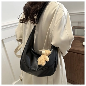 Detail of black semi-circle PU leather bag with cute plush bear charm on shoulder