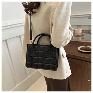 Detail of a black quilted handbag with gold hardware and adjustable strap on a model