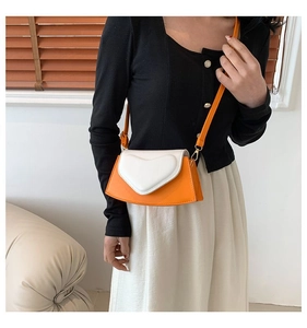 Detail of orange crossbody bag featuring a white heart-shaped flap and slim strap