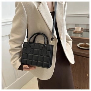 Detailed view of black quilted crossbody bag with gold hardware on a beige blazer