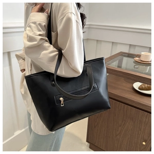 Detail of minimalist black leather tote bag with gold zipper outer pocket for work