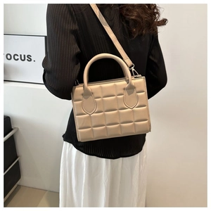 Detail of beige quilted crossbody bag with adjustable strap worn by a female model