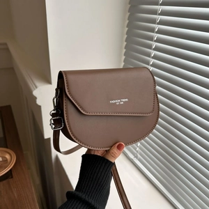Brown leather saddle bag with adjustable strap and fashion lettering on a neutral background
