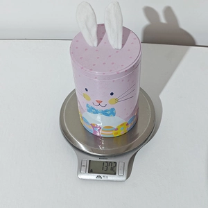 Pink rabbit tin box weighing 137.2g on an electronic scale for Easter candy storage