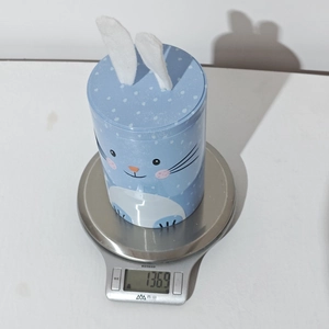 Close-up of Easter bunny tin box with plush ears on a scale showing 136.9g weight