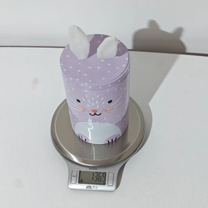 Weight measurement of purple bunny tin jar with plush ears on a digital scale