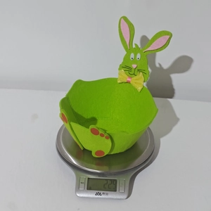 Green Easter felt bunny basket with yellow bow detail being weighed on a digital scale