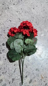Detalle de geranios artificiales de seda roja con hojas verdes de textura realista
