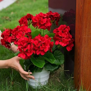Vibrantes geranios rojos artificiales en maceta blanca texturizada sobre césped
