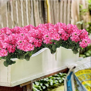 Geranios artificiales rosas en una jardinera rectangular de madera blanca con bordes