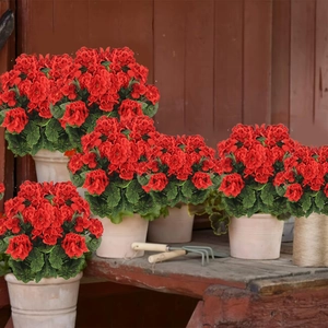 Detalle de geranio artificial rojo en maceta blanca sobre un banco de jardín