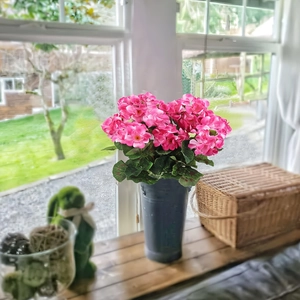 Geranios de seda rosa en un jarrón cilíndrico gris en un alféizar de madera