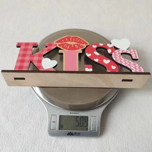Detailed view of KISS wooden sign with heart patterns on a scale weighing 50.9 grams