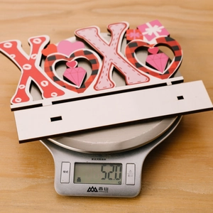 Balance de cuisine montrant le poids de 52g d'un décor en bois XOXO de la Saint-Valentin