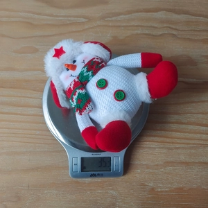 Detail view of a plush Christmas snowman ornament being weighed on a digital scale
