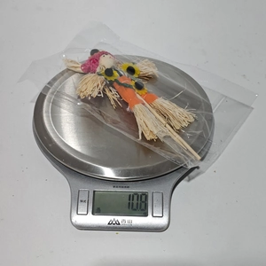 Makroaufnahme einer Stroh-Vogelscheuche mit orangefarbenem Stoff auf einer Küchenwaage