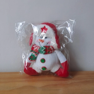 Detail view of a plush snowman doll with red star hat and scarf in clear packaging