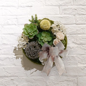 Detail of floral wreath with succulents, roses, and a silver sequin bow on white wall
