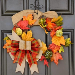 Close-up of autumn harvest wreath with maple leaves and pumpkins on gray wood door
