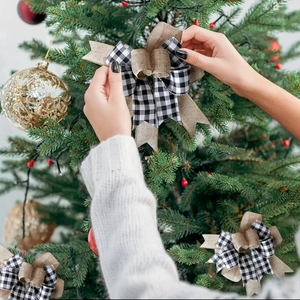 Close-up of hand placing a black and white plaid linen bow on a green Christmas tree