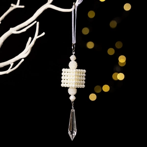 Detailed view of handmade pearl ornament with a transparent crystal pendant and white ribbon