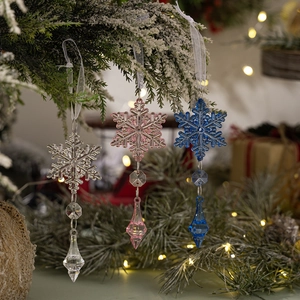 Close-up of snowflake crystal ornaments in pink and blue on snowy pine branches