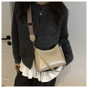 Detail of light beige glossy crescent crossbody bag with woven texture strap and gold hardware