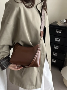 Brown leather square handbag with stylish geometric wide strap worn with a trench coat