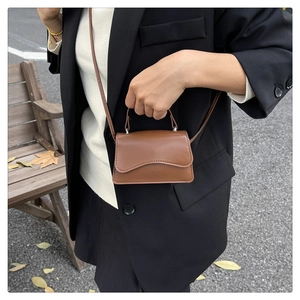 Mini brown crossbody bag with wave flap design worn outdoors by a model on a street