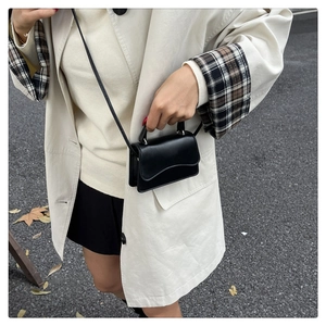 Detail view of a black minimalist crossbody bag with unique wave edge flap design