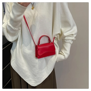 Close-up of red mini crossbody bag with wavy flap design on cream oversized sweater