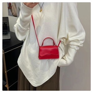 Close-up of a mini red leather crossbody bag with elegant wavy flap and top handle