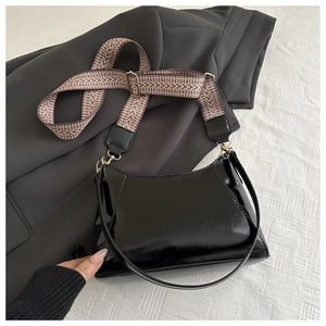 Detail der schwarzen Lackleder-Schultertasche mit gewebtem Riemen und goldener Hardware